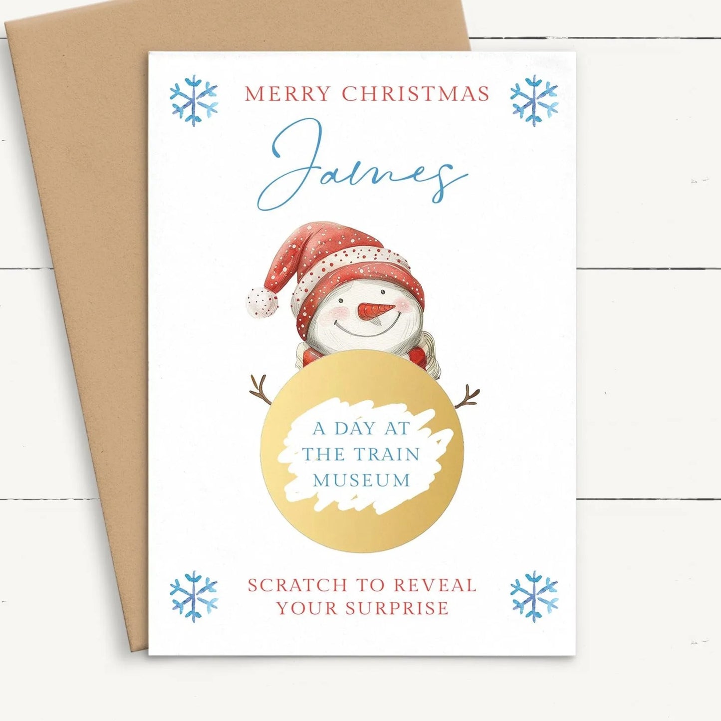 A Christmas card featuring a snowman with a golden ball, surrounded by snowflakes, and the text "Merry Christmas James" and "A day at the train museum" along with a prompt to "Scratch to reveal your surprise".