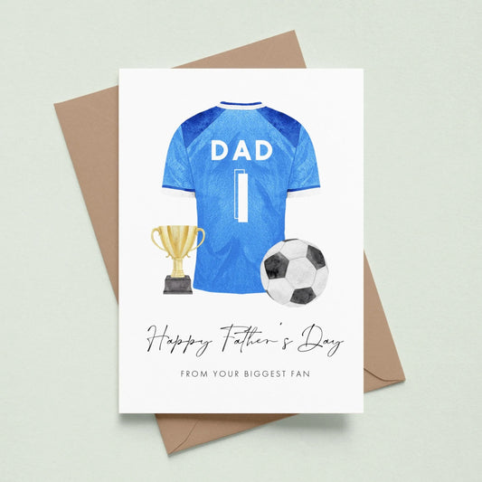 A greeting card with a blue soccer jersey, a trophy, and a soccer ball, along with the text "Happy Father's Day" and "From your biggest fan" printed on it.