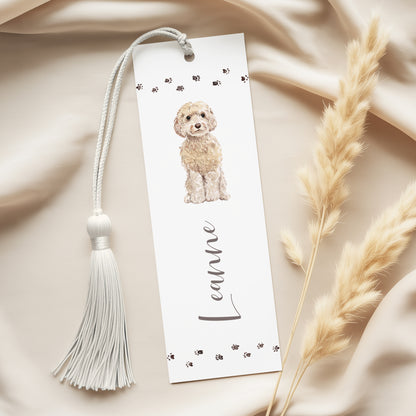 A white bookmark with a tassel and a picture of a small dog on it, placed on a beige fabric surface.
