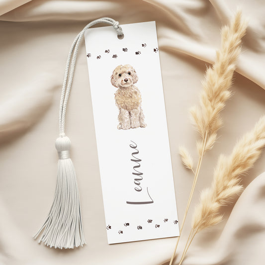 A white bookmark with a tassel and a picture of a small dog on it, placed on a beige fabric surface.