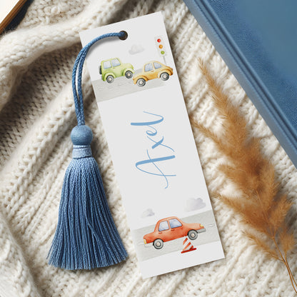 A white bookmark with a blue tassel and illustrations of two cars on a road, along with the name "Axel" written on it.
