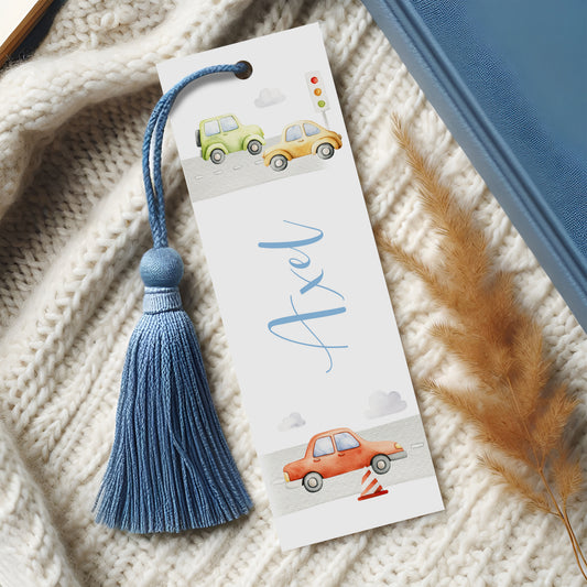 A white bookmark with a blue tassel and illustrations of two cars on a road, along with the name "Axel" written on it.