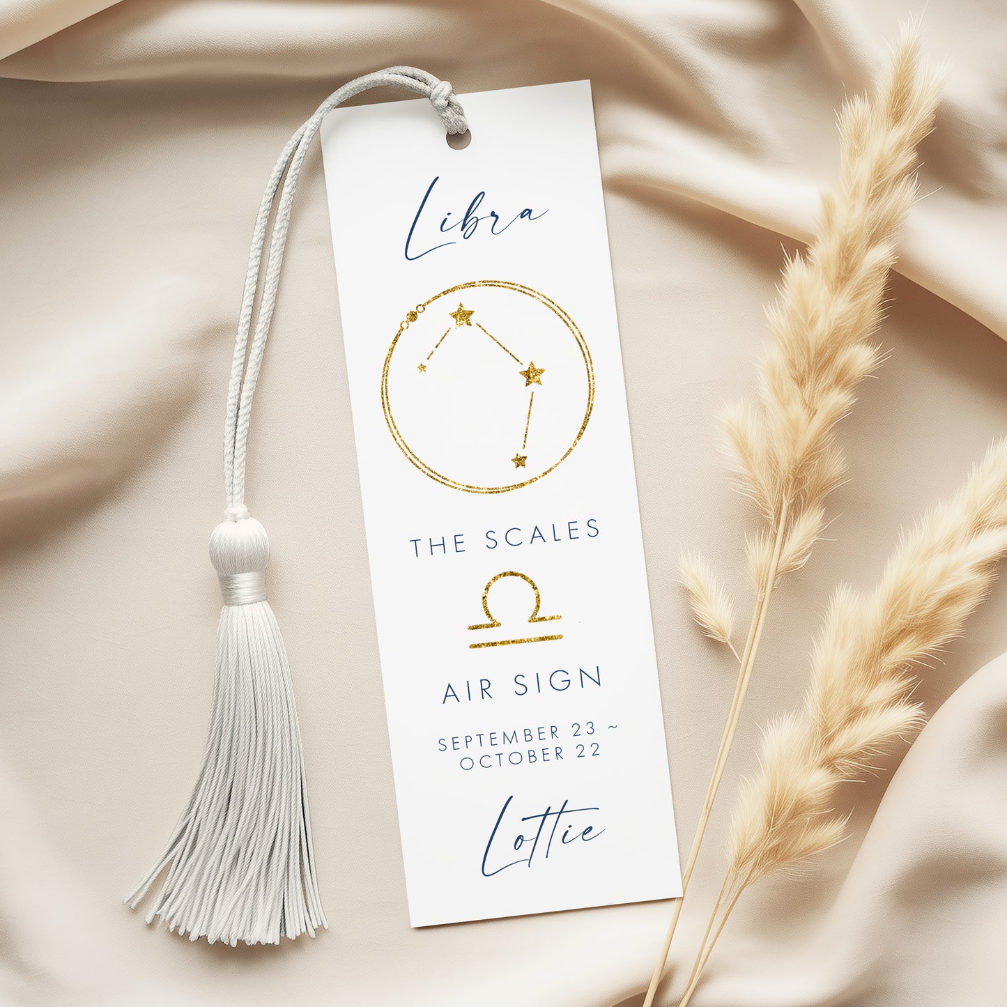 A white bookmark with a tassel and a gold astrological symbol for Libra, along with the text "The scales air sign" and "Lottie" printed on it.
