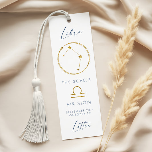 A white bookmark with a tassel and a gold astrological symbol for Libra, along with the text "The scales air sign" and "Lottie" printed on it.