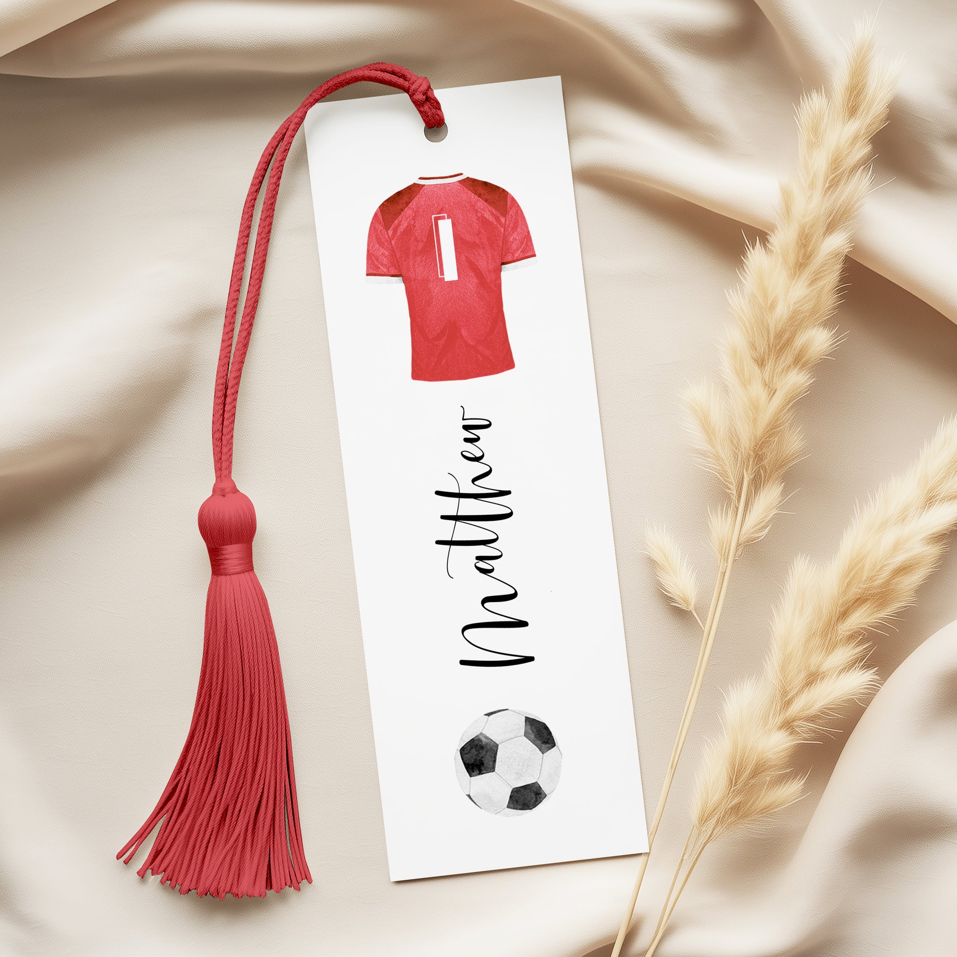 A personalized bookmark with a red tassel and a soccer ball design, along with a name tag.