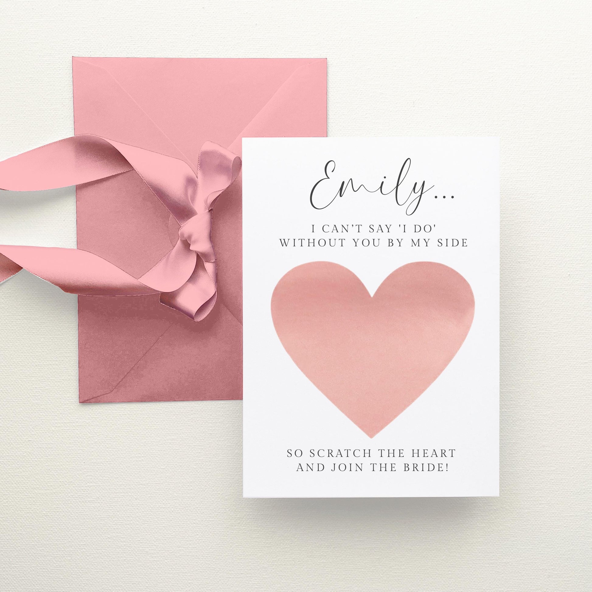 a pink envelope with a heart-shaped scratch-off card attached to it, along with a pink ribbon.