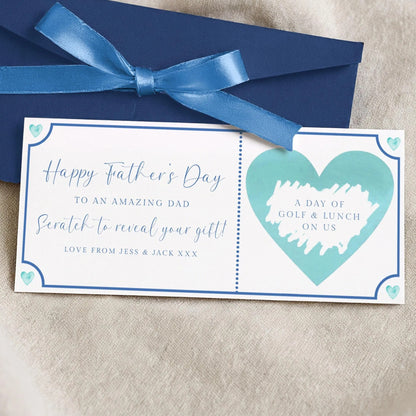 A blue envelope with a blue ribbon and a white card with a blue heart and text on it, placed on a beige surface.