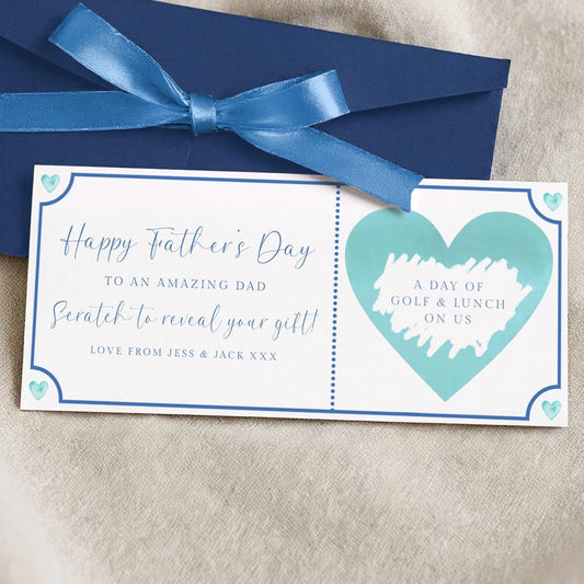 A blue envelope with a blue ribbon and a white card with a blue heart and text on it, placed on a beige surface.