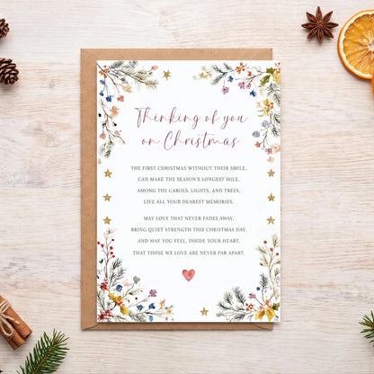 a Christmas card with a floral design, surrounded by holiday decorations such as pine cones, oranges, and holly leaves.