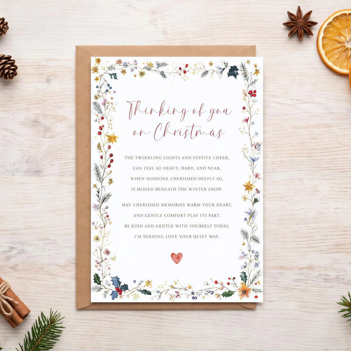 a Christmas card with a floral border, surrounded by holiday decorations such as pine cones, oranges, holly leaves, and pine needles.