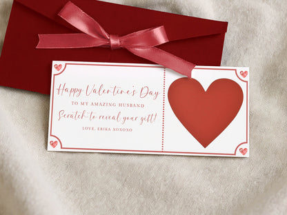 a Valentine's Day card with a red ribbon and a heart-shaped scratch-off ticket, placed on a beige fabric background.