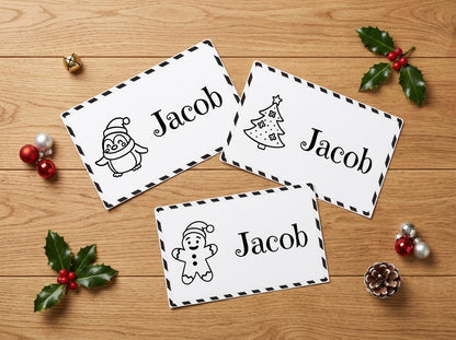 three name cards with the name "Jacob" written on them, along with illustrations of a penguin, a Christmas tree, and a gingerbread man. The cards are placed on a wooden surface, surrounded by holiday decorations such as holly leaves, berries, and ornaments.