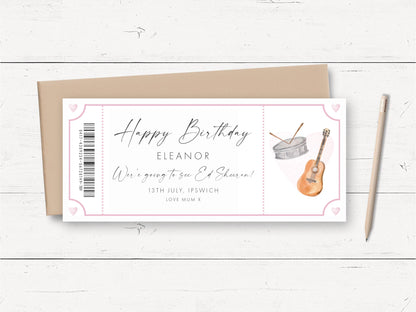 A birthday card with a guitar and drum on it, along with a pencil and a brown envelope on a white wooden surface.