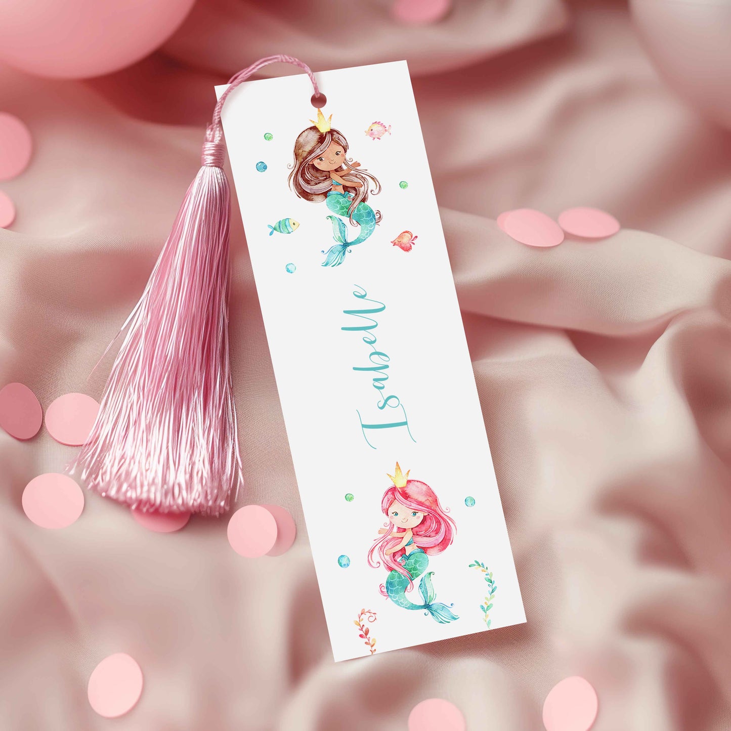 A white bookmark with illustrations of mermaids and the name "Isabelle" printed on it, along with a pink tassel.