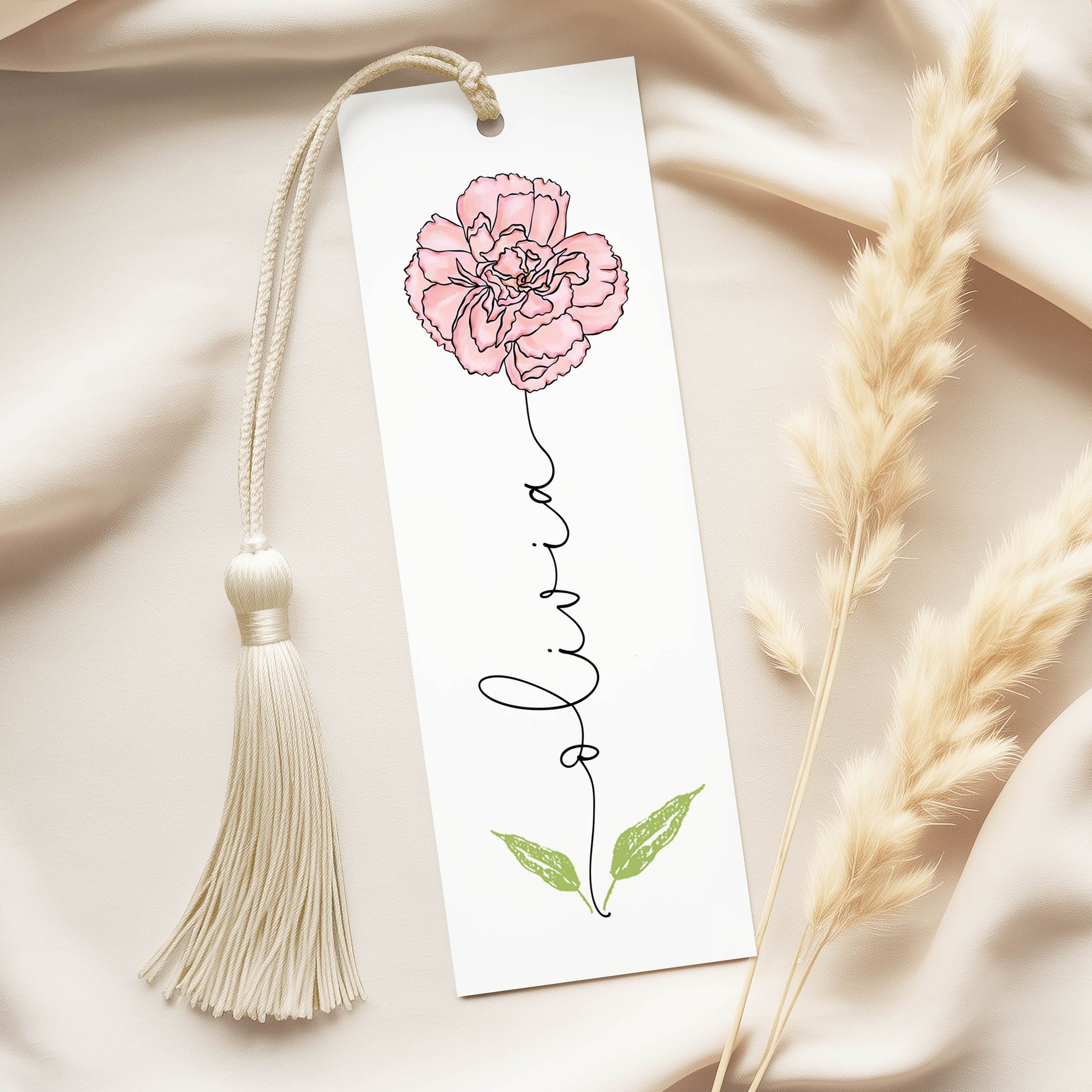 A white bookmark with a pink flower illustration and the name "Livra" written on it, along with a white tassel.