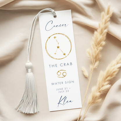 a white bookmark with a tassel and a cancer-related design, placed on a beige fabric background.